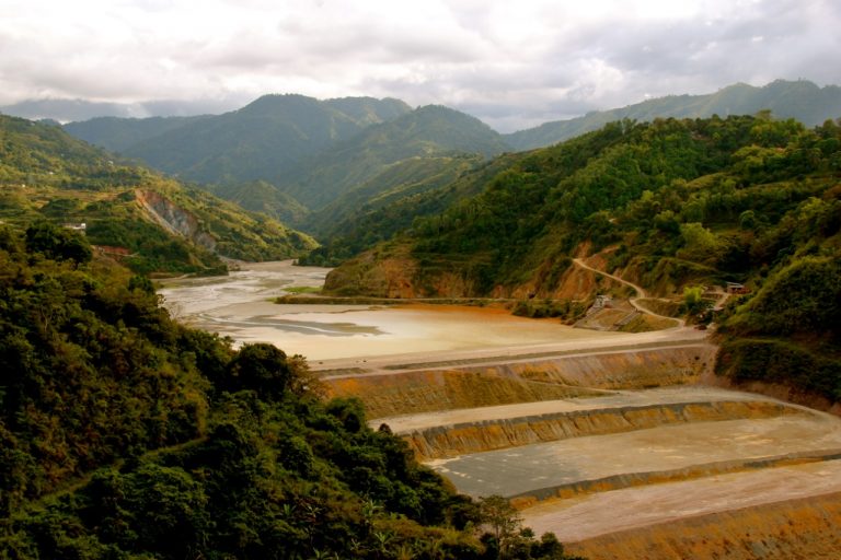 Barragem de rejeitos de mineração com mata verde e montanhas ao fundo