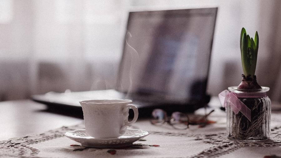 Imagem de um computador e uma xícara de café em um ambiente caseiro exemplificando o Home Office